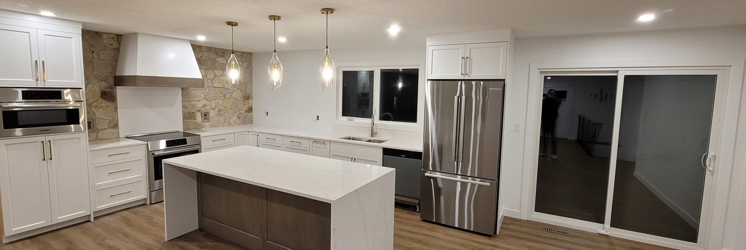 Whole home renovation in Edmonton with a new open concept kitchen, white shaker cabinets, quartz waterfall island, and a stone feature wall