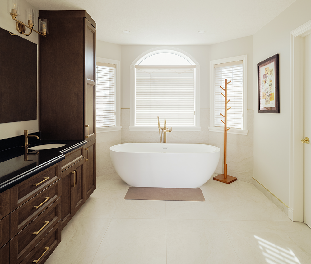 Renovated primary bathroom with a freestanding tub, dark wood vanity, brass fixtures, and an arched window
