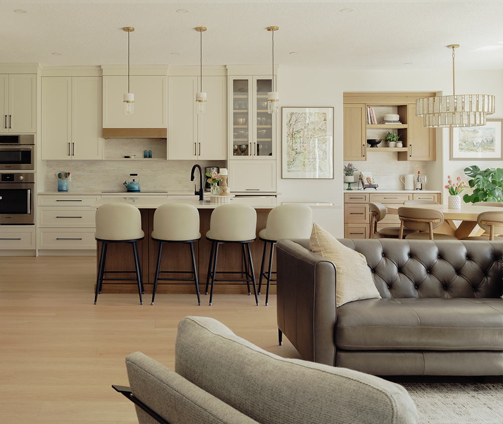 Open concept main floor renovation with a kitchen, dining area, and living room, featuring cream cabinets, a large island, and a tufted leather sofa
