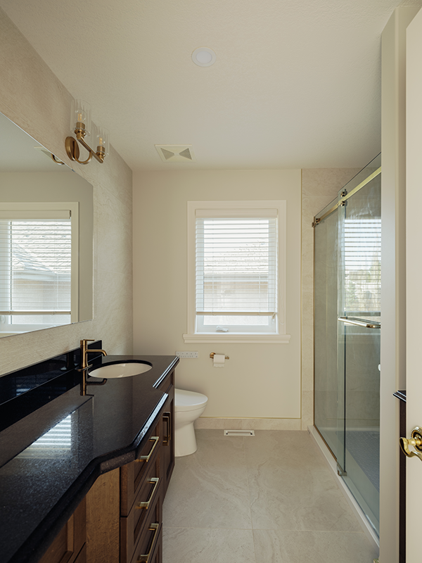 Renovated bathroom in Edmonton with a dark wood vanity, black granite countertop, brass faucet, and glass shower enclosure.
