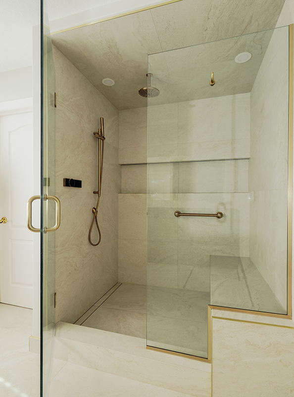 Interior of a renovated walk-in shower with marble tile walls, brass slide bar, hand shower, grab bar, and linear drain.