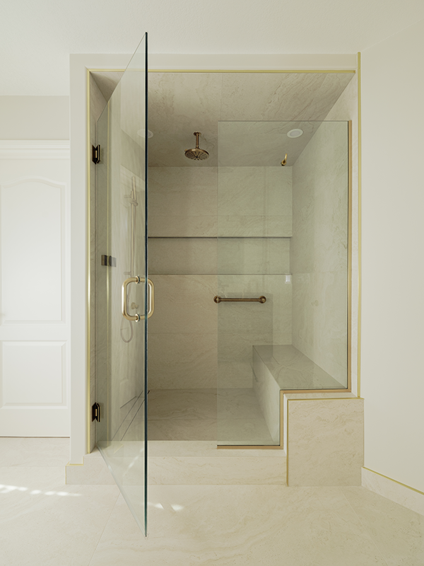 Walk-in shower in an Edmonton bathroom renovation with large-format marble tile, brass-framed glass door, built-in bench, and rain head.