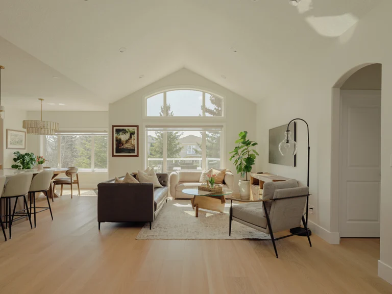 Open-concept main floor with a vaulted ceiling joining the living room, dining area, and kitchen, lit by a large arched window in Edmonton.
