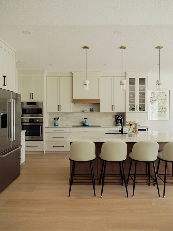 Wide-angle kitchen view with cream shaker cabinets, a walnut island, cushioned bar stools, and brass-capped pendant lighting.