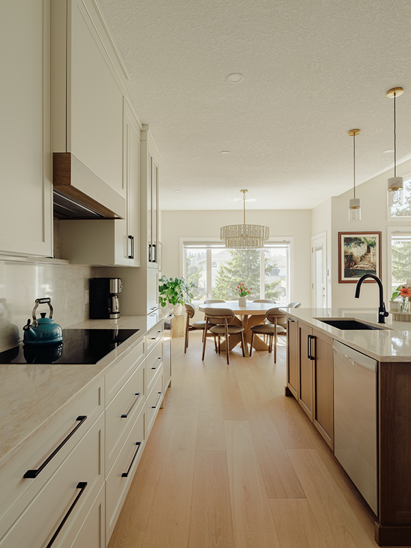 Renovated open concept kitchen with cream cabinets and a walnut island, leading to a round dining table beneath a glass chandelier.