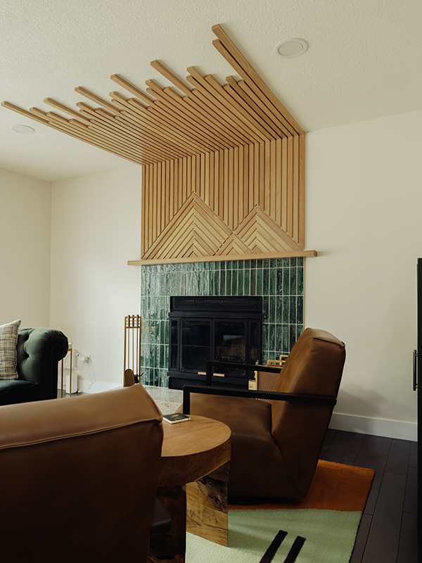 Renovated Edmonton living room with a custom wood slat fireplace surround, geometric mantel detail, green zellige tile, green velvet sofa, and leather armchairs.