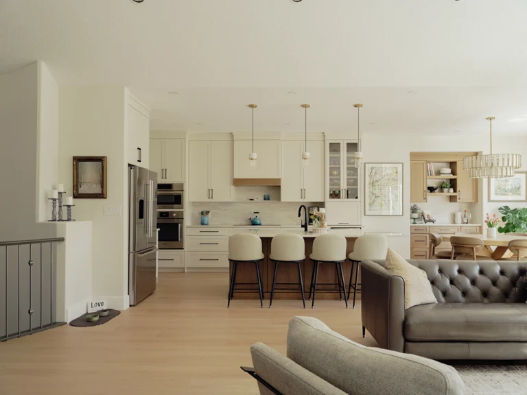 Open-concept main floor showing the two-tone kitchen, dining area, and living room with a tufted leather sofa and light hardwood floors.