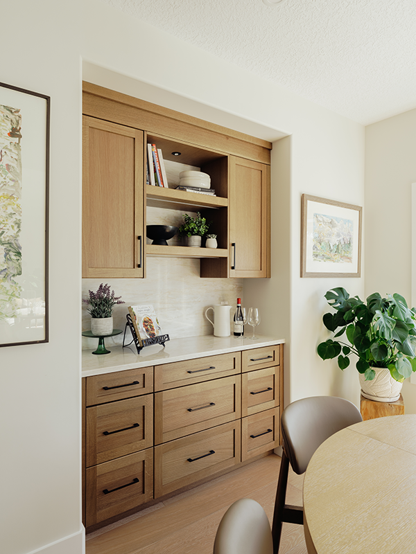 White oak butler pantry with shaker cabinets and open shelving, beside a framed print and a round dining table.