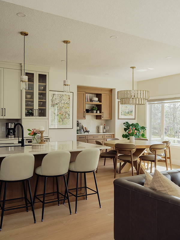 Wide-angle view of an open-concept kitchen and dining space with two-tone cabinets, bar stools at a walnut island, and a brass drum chandelier over the dining table.