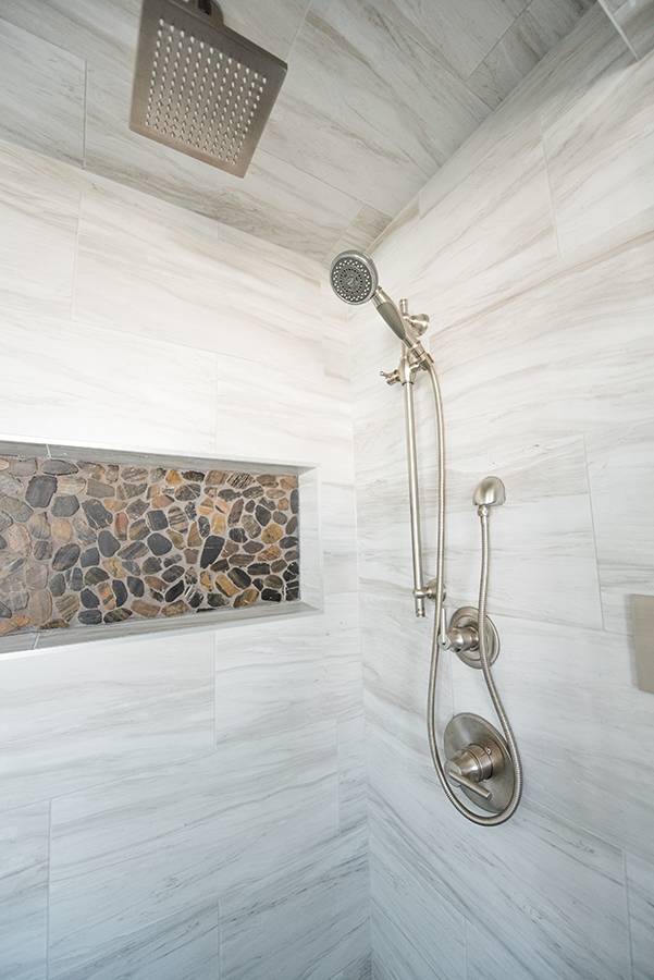 Detail of steam shower rain head, brushed nickel handheld fixture, and river rock niche in primary ensuite — Edmonton second-story addition