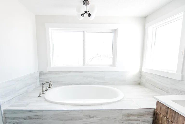 Drop-in soaker tub with marble-look tile surround and large windows flooding the primary ensuite with natural light — Ermineskin home addition
