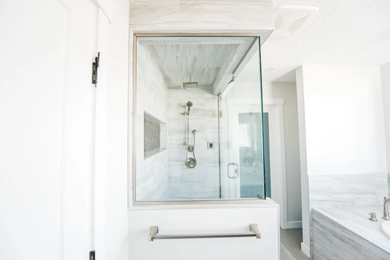 Glass-enclosed steam shower with marble-look tile walls, rain head, and river rock niche — primary ensuite in Edmonton home addition