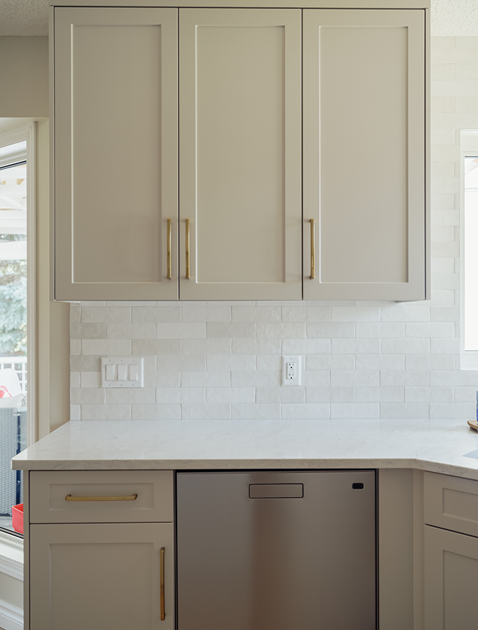 Upper cabinets with gold hardware and white tile backsplash above dishwasher — kitchen renovation in Spruce Grove, AB