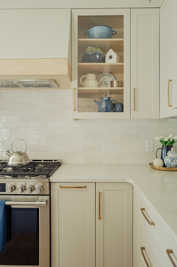 Glass-front upper cabinet beside gas range, maple hood valance, and white glossy tile backsplash — kitchen renovation in Spruce Grove, AB
